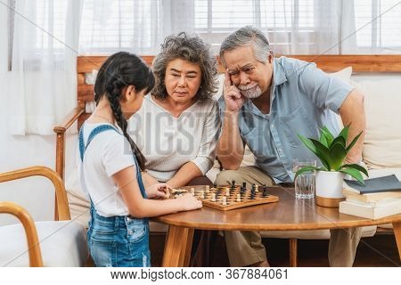 Asian Couple Grandparent With Grandchild Playing The Chess With Use Thought Together, Support And Su
