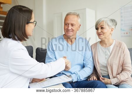 Portrait Of Smiling Senior Couple Shaking Hands With Female Doctor While Visiting Private Clinic