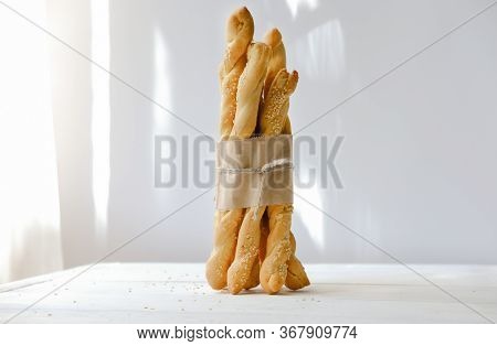 Italian Grissini Or Salted Breadsticks. Sesame Breadsticks In A Craft Paper On White Wooden Table. C