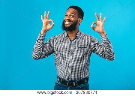 Im Fine. Close Up Portrait Of Happy African Business Man Doing Ok Gesture Isolated Over Blue Studio 