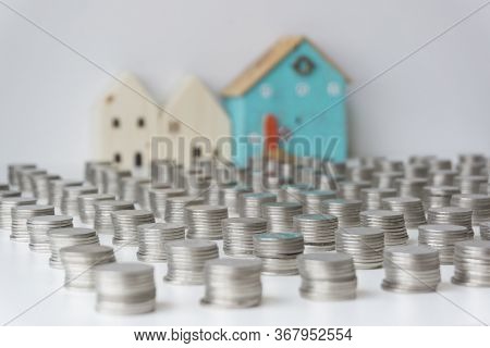 Silver Coins Are Stacked In A Row And The 3 Small Houses Are At The Back. Concept Of Saving Money To