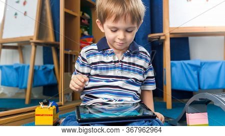 Portrait Of Happy Smiling Little Boy Watching Cartoons On Digital Tablet Computer In His Room