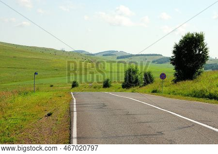 A Two-lane Asphalt Road Curves Through A Picturesque Hilly Valley On A Warm Summer Day.