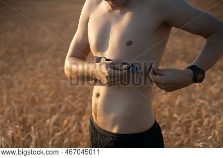 An Athletic Young Man Warms Up Outdoors, Puts On A Heart Rate Monitor And Prepares For An Active Run