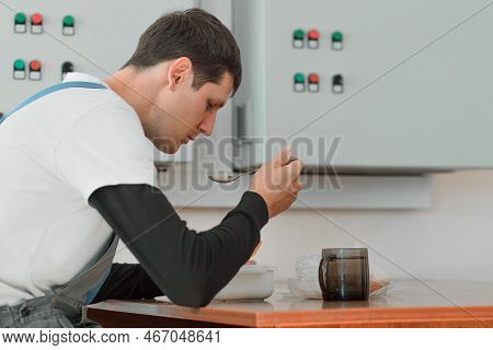Lunch Break. Eating In Workplace During Work. Caucasian Man In Work Suit Sits At Table In Production