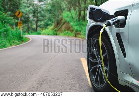 Electric Car Or Ev Car Charging In Station On Asphalt Road In Morning Time Background. Eco-friendly 