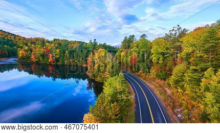 Aerial Over Road Next To Blue Lake And Surrounded By Fall Forest
