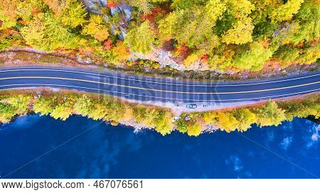 Aerial Looking Down On Road Between Blue Water Lake And Rocky Forest In Fall