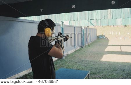 Asian Shooter Man Wearing Noise Canceling Headphones And Black Clothes Practicing Shooting Rifle At 