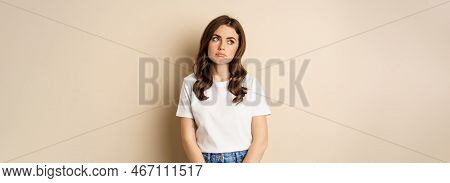 Sad And Tired Brunette Woman Looking Drained And Unamused, Standing With Pokerface Against Beige Bac