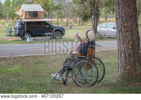 Asian Female Tourists Sitting In A Wheelchair And Drinking Water From A Bottle, At The Tent Camping 