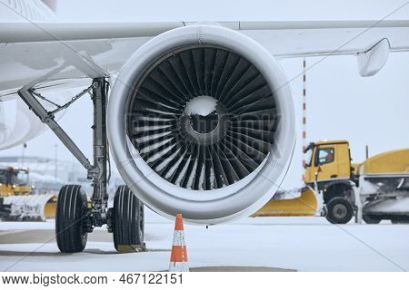 Winter Day At Airport During Snowfall. Snowy Jet Engine Of Airplane. Snowplows Clearing Snow From Ru