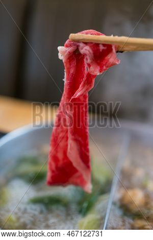 Hand Using Chopsticks Pick Raw Fresh Beef Over The Hot Pot Soup For Shabu Shabu Dipping And Dropping