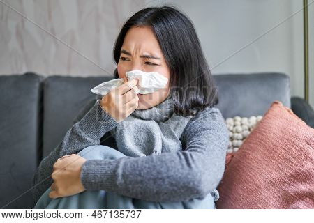 Close Up Of Korean Girl Sneezing In Napking, Sitting At Home In Scarf, Feeling Unwell, Concept Of Wi