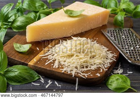 Shredded Parmesan Cheese And Grater On A Cutting Board. Grana Padano Cheese Whole Wedge And Grated, 