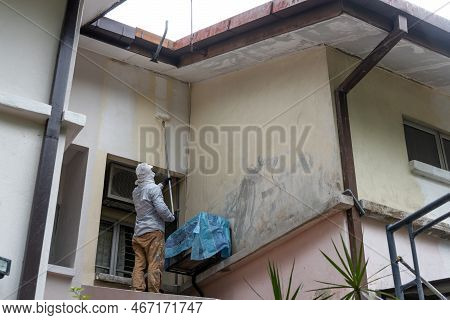 Painter Worker Adding Undercoat Foundation Paint Onto Wall With Roller At Residential Building In Re