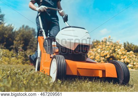 A Young Man In A Straw Hat Is Mowing A Lawn With A Lawn Mower In His Beautiful Green Floral Summer G