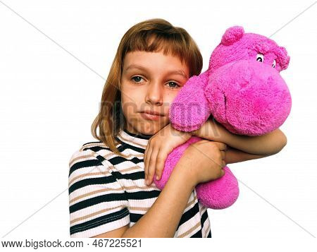 A Cute Caucasian Girl Of 7 Years Old With Blond Hair Cuddles And Hugs A Pink Hippopotamus. Hippo Plu