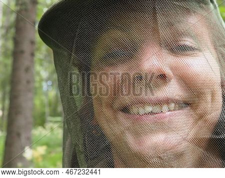 A Woman In Her 40s Wearing A Mosquito Headdress Smiles And Looks At The Camera. Cap And Mesh Against