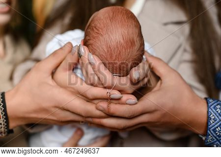 Sacrament Of Baptism Of A Baby In The Church, Parents Holding The Babys Head And A Cross.