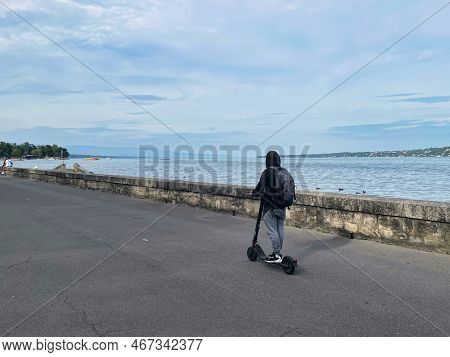 Geneva, Switzerland - September 14 2021: A Black Hooded Person Is Riding On An Electric Scooter Alon