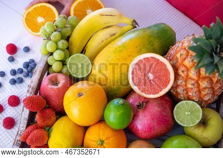 Close-up On A Wooden Basket Full Of Colorful Fresh Fruit. Mature Woman's Hands Holding Half A Orange