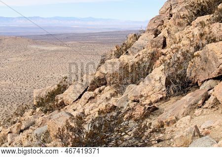 Creosote Plants Besides Granite Rocks On An Arid Mountain Ridge Overlooking The High Desert Plain Ta