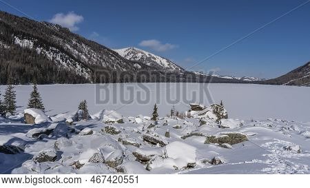 A Chain Of Footprints Is Visible On The Flat Snow-covered Surface Of The Frozen Lake. Surrounding Mo