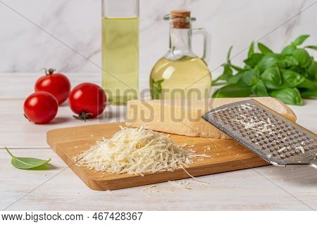Heap Of Grated Parmesan On A Cutting Board. Grana Padano Cheese Whole And Grated, Hand Grater, Olive