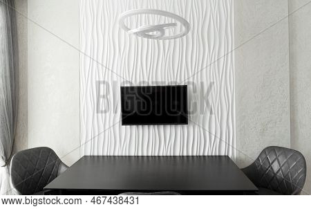 Minimalist Interior. A Large Glass Table With Chairs Against A Structural White Wall With A Tv In Th