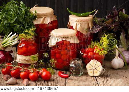 Canned Tomatoes In Closed Jars With Spices On A Wooden Background. Harvesting Tomatoes For The Winte