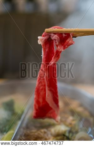 Hand Using Chopsticks Pick Raw Fresh Beef Over The Hot Pot Soup For Shabu Shabu Dipping And Dropping