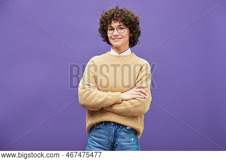 Young Smiling Brunette Woman In Eyeglasses, Blue Jeans And Beige Knitted Pullover Crossing Arms By C