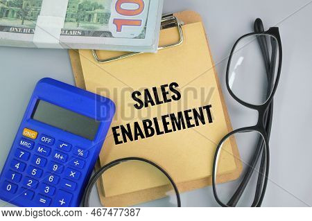 Paper Money, Glasses, Calculator, Magnifying Glass And Paper With The Word Sales Enablement