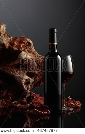 Bottle And Glass Of Red Wine. In The Background Old Driftwood And Dried-up Vine Leaves. Frontal View