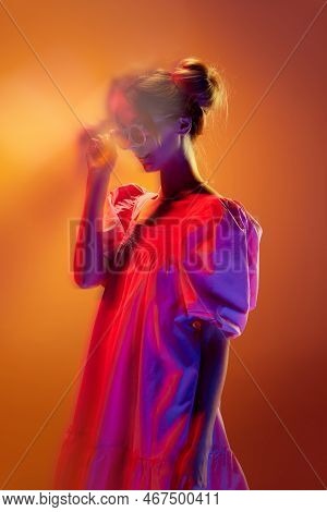 Portrait Of Young Stylish Girl In White Dress Posing Over Orange Background In Neon Lights. Unfocuse