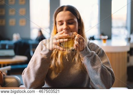 Portrait Of A Joyful Teengirl Enjoying A Cup Of Tea At Cafe. Smiling Beautiful Girl Drinks Hot Tea I