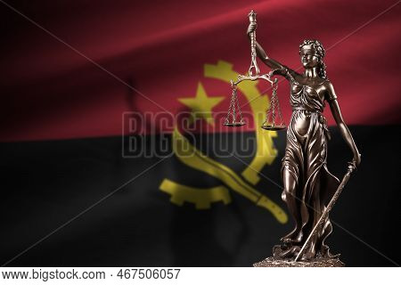 Angola Flag With Statue Of Lady Justice And Judicial Scales In Dark Room. Concept Of Judgement And P