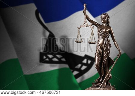 Lesotho Flag With Statue Of Lady Justice And Judicial Scales In Dark Room. Concept Of Judgement And 