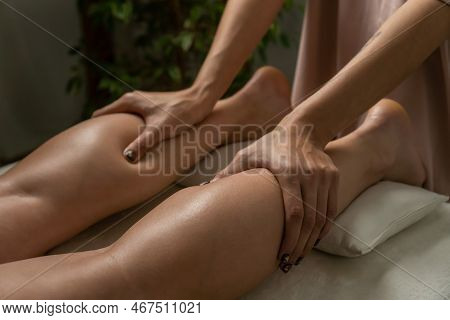 Masseur's Hands Massage The Legs And Calves Of A Young Woman In A Spa Salon In A Cozy Warm Atmospher
