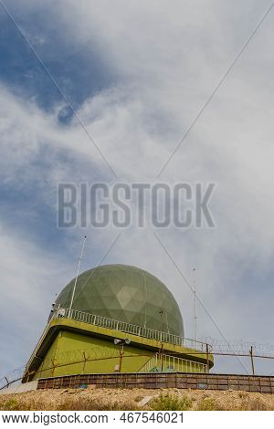 Communications And Radar Dome On Hill Under Cloudy Sky.