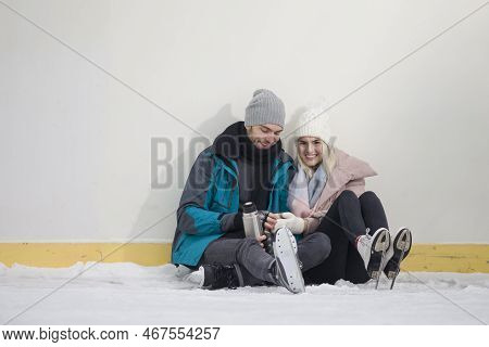 Young Caucasian Couple In Love In Winter With Ice Skates Posing Together With Vacuum Flask In Snowy