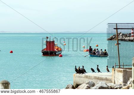 Struisbaai, South Africa - Sep 21, 2022: A Fishing Boat And A Dinghy With People Rowing At The Harbo