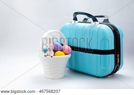 Happy Easter, Rabbit Standing In White Ceramic Basket With Decorated Eggs And Small Blue Travel Bag.
