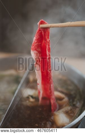Chopsticks Holding Raw Fresh Beef Shabu-shabu To Pot With Hot Soup. Japanese Shabu-shabu Or Sukiyaki