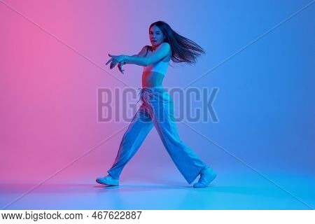Young Stylish Girl Dancing Hip-hop Over Gradient Pink Blue Background In Neon Light. Dynamic Steps