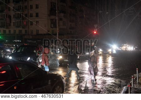 Kyiv, Ukraine - Dec. 16, 2022: Passers-by Cross The Street At A Pedestrian Crossing Illuminated By C