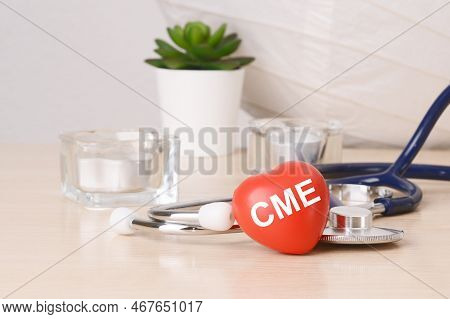 The Word Cme Is Written On Red Heart Shaped Toy On On Wooden Table Near A Stethoscope On Background