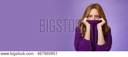 Gloomy Upset Redhead Girlfriend Pulling Collar Of Purple Sweater On Nose, Frowning And Squinting Off