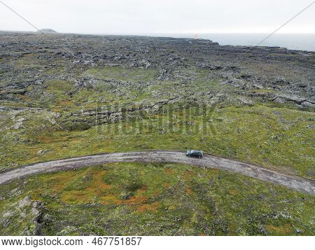 Rocky Volcanic Highland And A Road With One Lonely Car Driving On It - Iceland